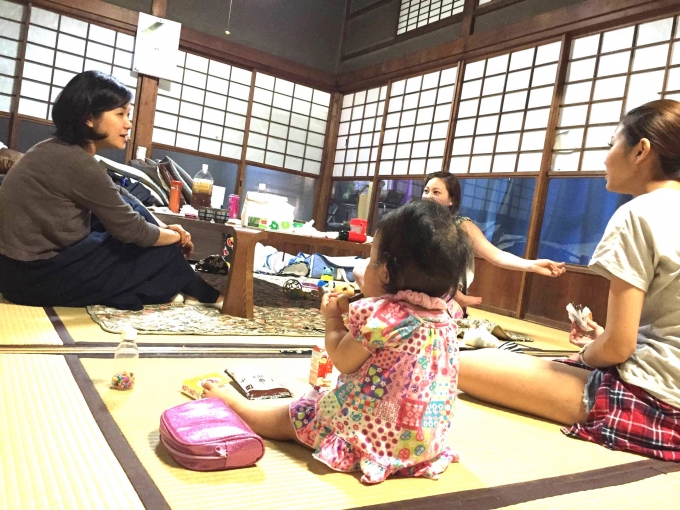 【写真】畳の部屋であたたかい雰囲気で机を囲む女性。側では赤ちゃんが遊んでいる。