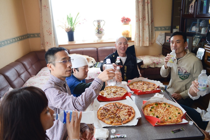 【写真】6人ほどがピザを食べている。トリトンはのぶさんの近くのソファで見守っている