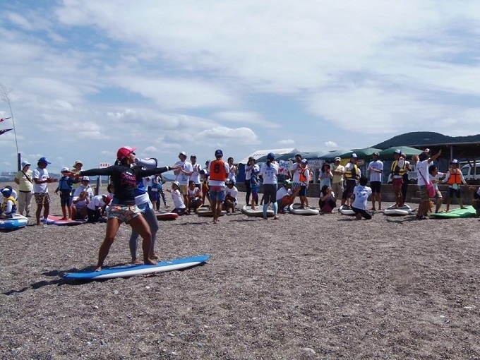 【写真】安全講習を砂浜で行う様子。砂浜に置かれたサーフィンボードの上で立つ練習をしている