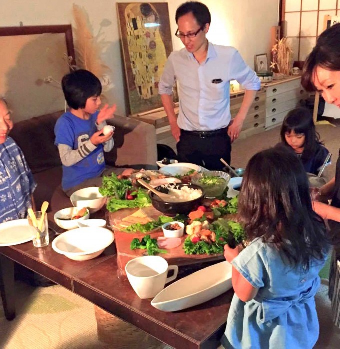 【写真】食卓を囲むように大人と子供が数人おり、様々な料理が並んでいる。