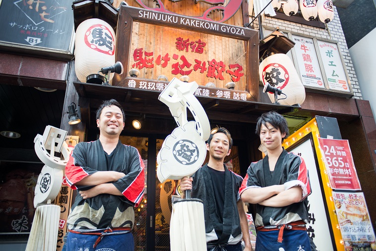 【写真】新宿駆け込み餃子と書かれた店表の看板の前で、従業員3人が笑顔で立っている。お店の装飾には提灯も使われ、賑やかな雰囲気