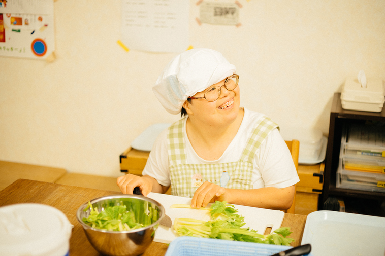 【写真】キッチンにて、笑顔で、野菜に調理を進めるメンバーさん。