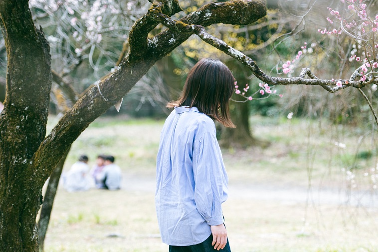 【写真】梅の木の下で、うつむき加減で歩く女性