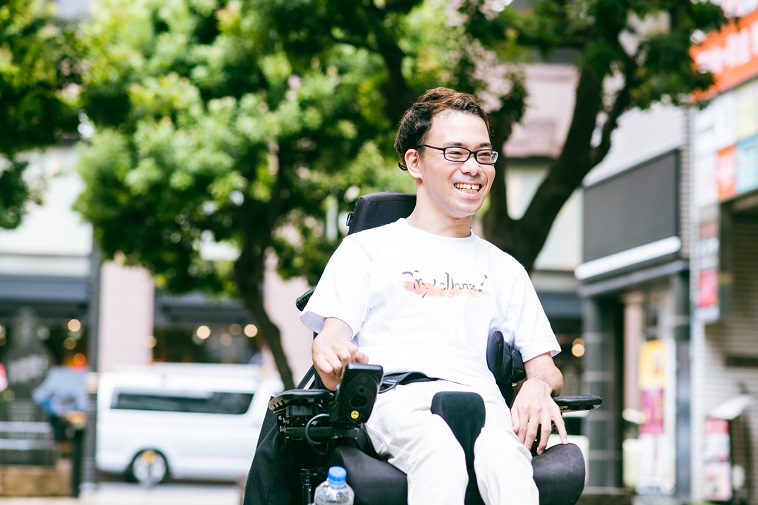 【写真】満面の笑みで街中を電動車椅子で移動するながのさん