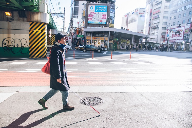 【写真】新宿の街中を白杖を持って歩くいしいけんすけさん