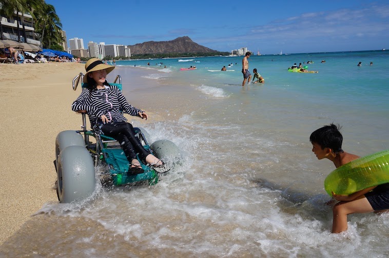 【写真】波打ち際で車椅子に乗って水遊びをするゆりこさん