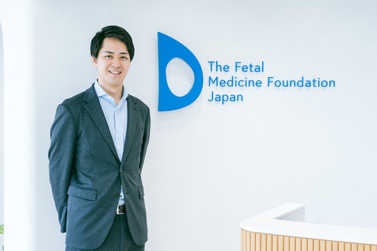 【写真】ご自身が運営する一般社団法人「FMF Japan」のロゴの前で笑顔を見せるはやしのぶひこさん
