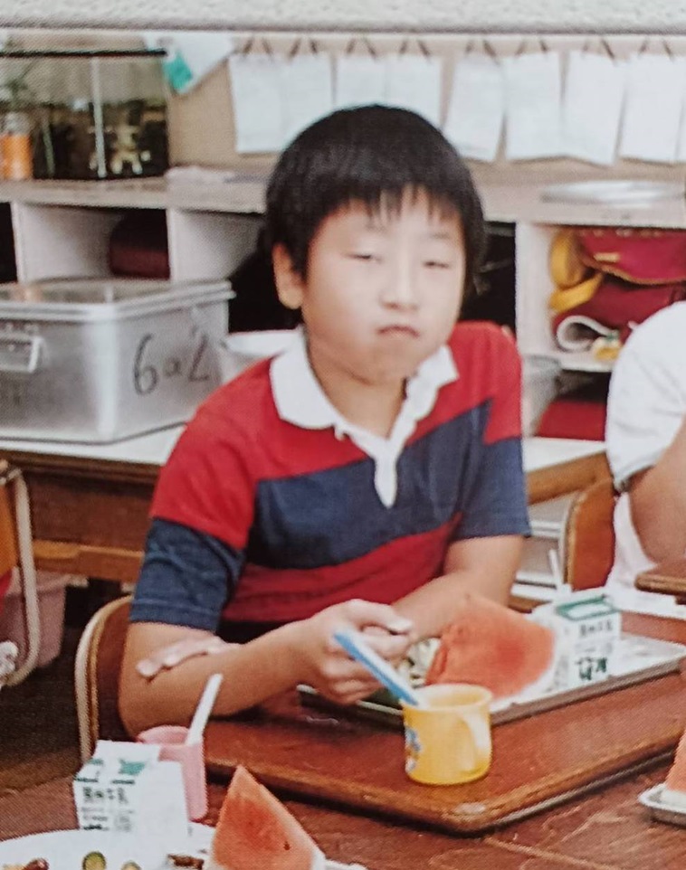 【写真】小学生の頃のなんばさん。無表情で給食を食べている。