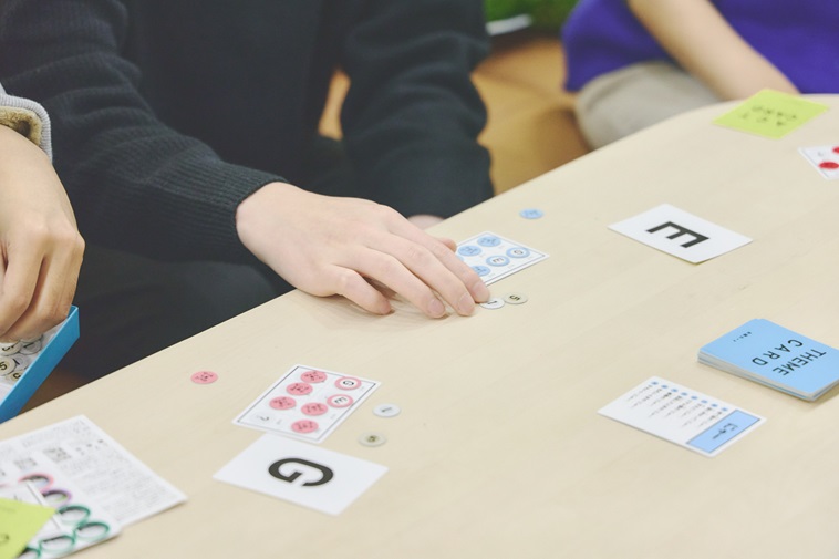 【写真】テーブルの上に置かれたカードゲームと、若者の手