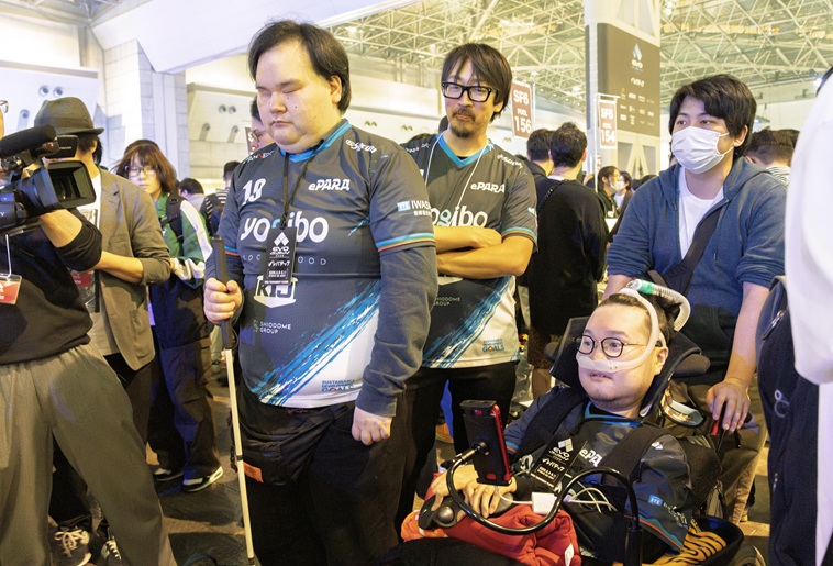 【写真】きたむらさんの後ろに車いすに乗ったはたけやまさんとePARAスタッフが続いて歩いている様子