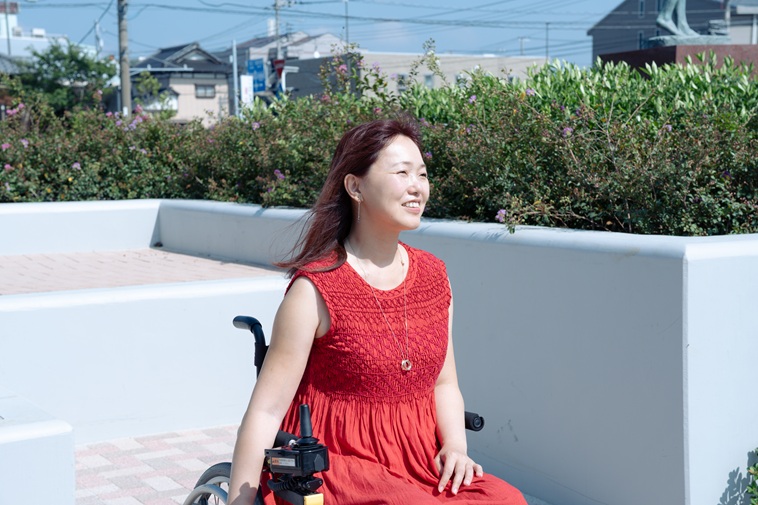 【写真】屋外で太陽の光に当たりながら微笑むおざわさん