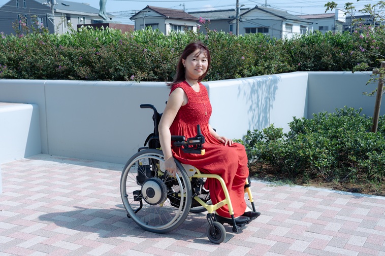 【写真】車いすに座り、カメラを見つめるおざわさん