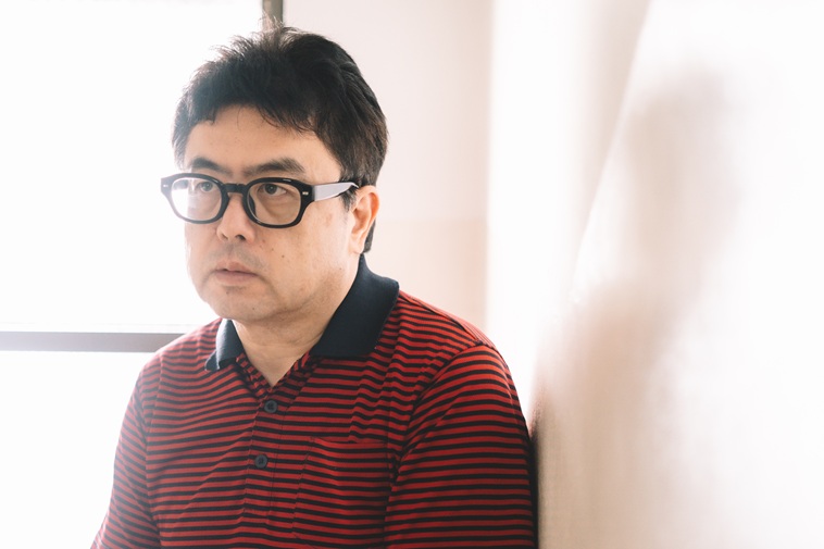 【写真】壁に寄りかかりながら左上の方向を見つめるきみづかたくみさん