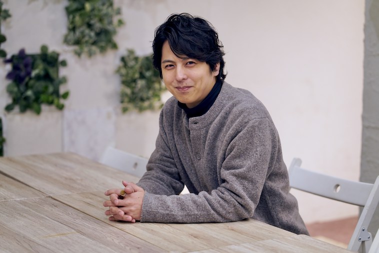 【写真】椅子に座りカメラを見つめて微笑むいわきりけんいちろうさん