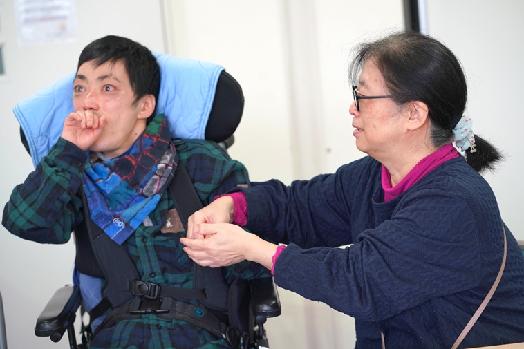【写真】ひでのりさんとみちこさん。ひでのりさんはみちこさんの手に指で文字を書いている