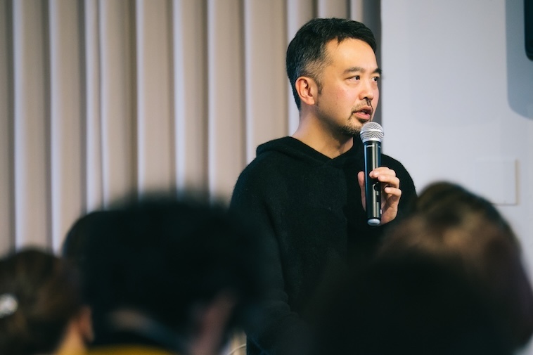 【写真】マイクを持ち、会場を見渡して話すドミニクさん