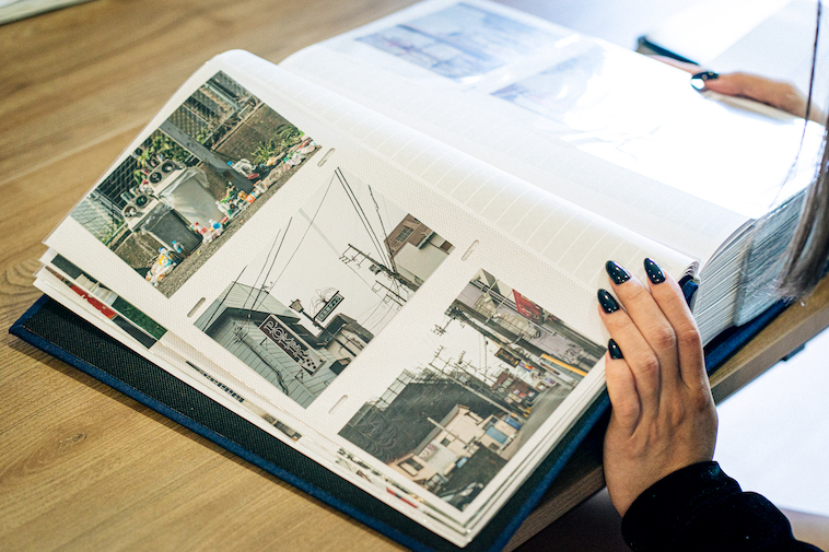 【写真】街並みが写る写真が並ぶアルバムをめくっている
