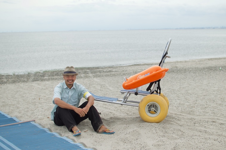【写真】砂浜に座る笑顔のにしださんとモビチェア