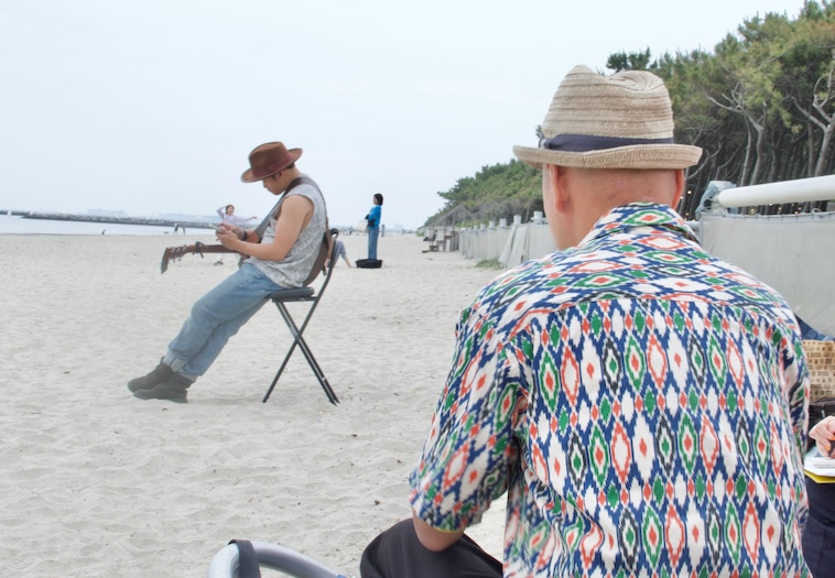 【写真】海辺でギターを弾く人のほうを向いているにしださん